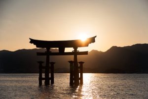 The iconic Itsukushima Shrine Torii Gate silhouetted against a stunning sunrise in Hiroshima, Japan.