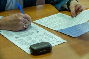 Close-up of a man filling out official documents with a pen on a wooden table.